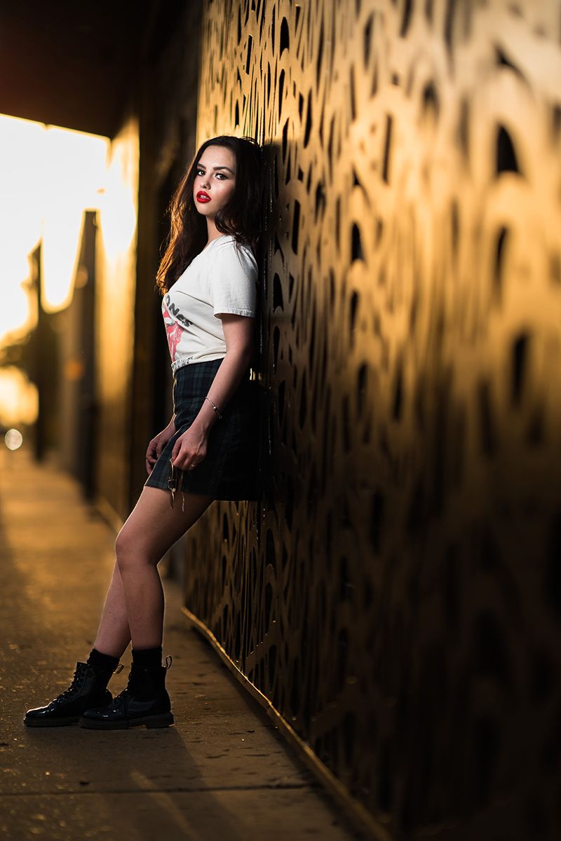 woman leaning on wall in white shirt and dark skirt.