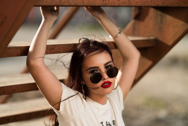 woman wearing sunglasses with red lipstick and white shirt holding onto metal stairs.