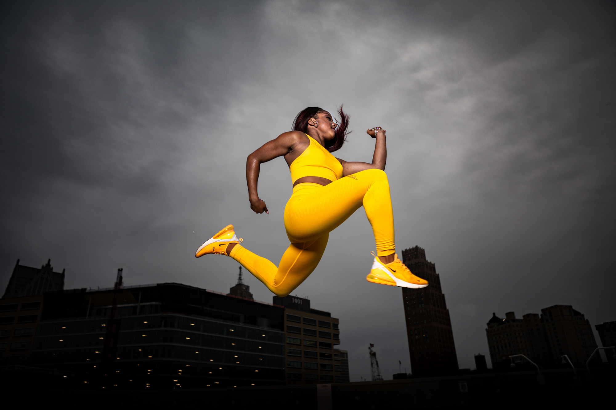 Young woman jumping in yellow suit under a dark sky